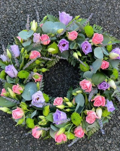 Wreath SYM-316 - A beautiful classic wreath arranged using purple and white flowers and finished with fine foliage.